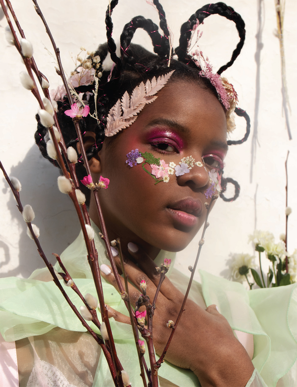 Image shows model with braids, and floral make-up looking into camera