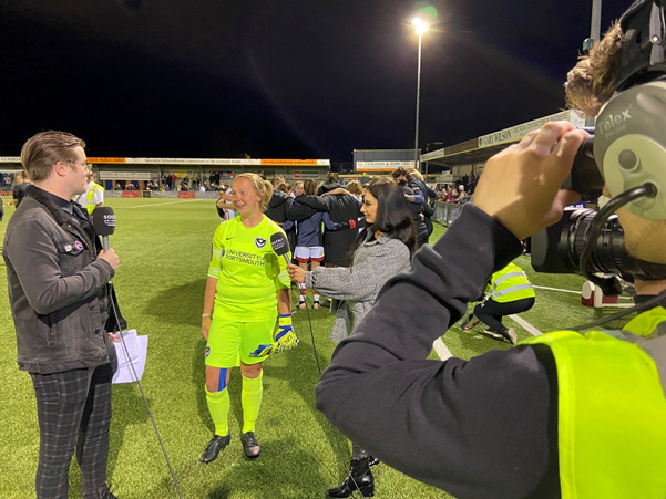 Image of students interviewing and filming football player on the pitch