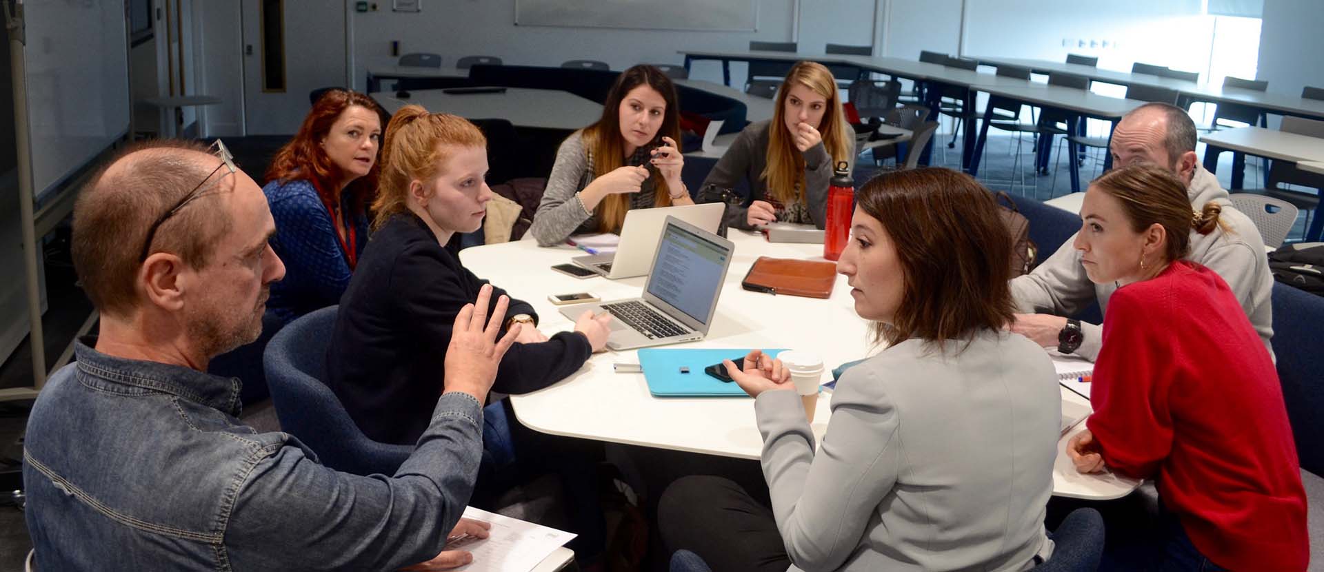 A group of students sitting round a table talking with lecturers