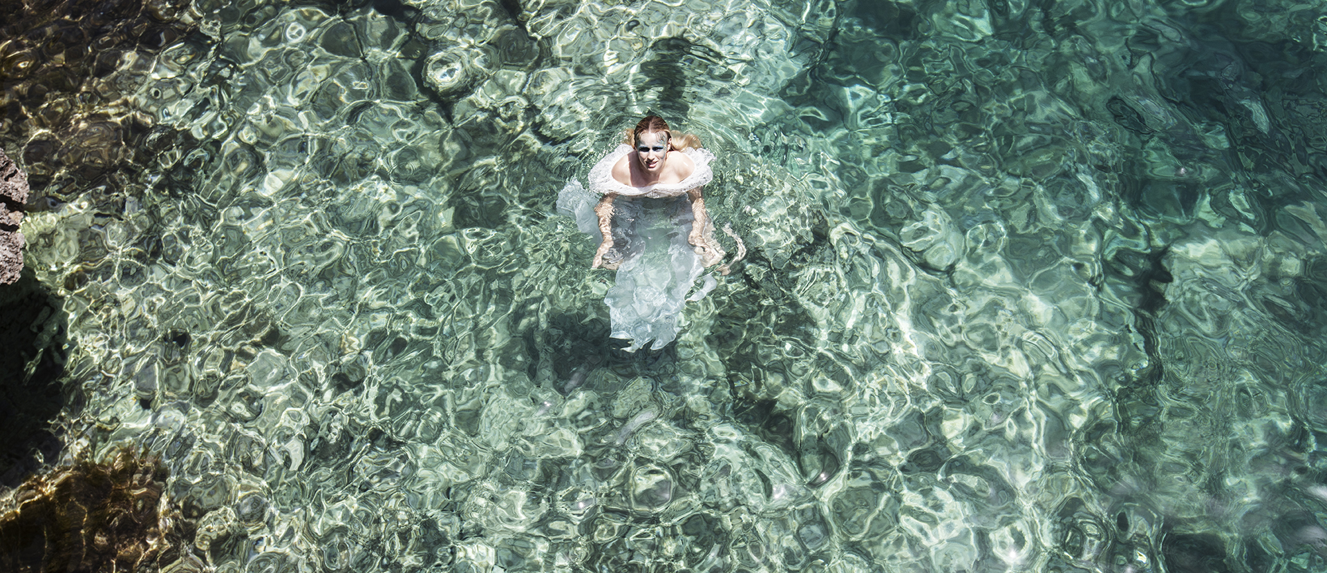 A female model wearing a white dress, standing in a pool of water