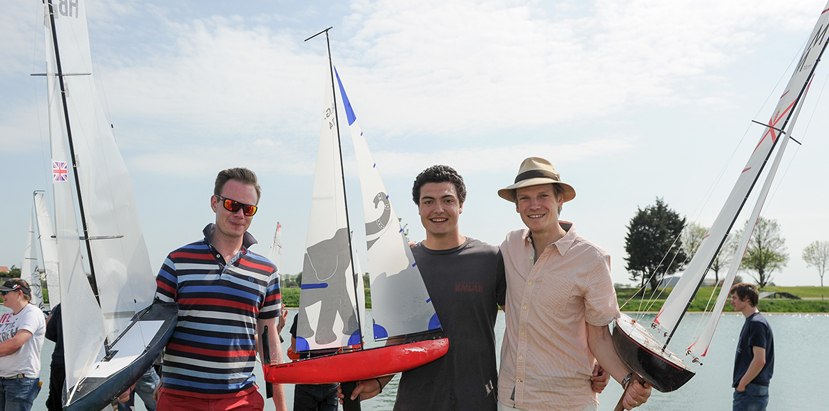 Three competitors at the annual model yacht race holding their yachts