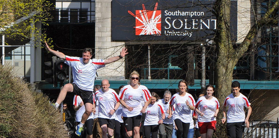 A group of people running outside the Solent University buildings