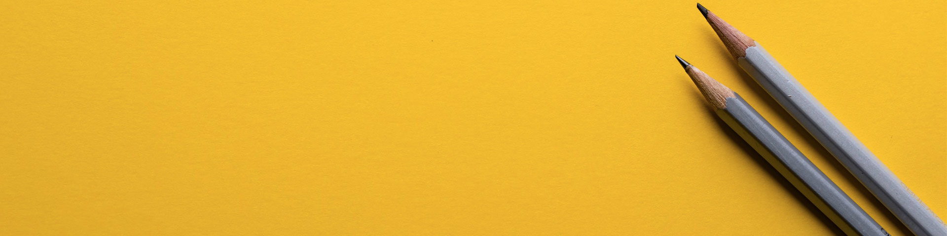 Two sharp grey pencils rest on the far right side of an all yellow backdrop.
