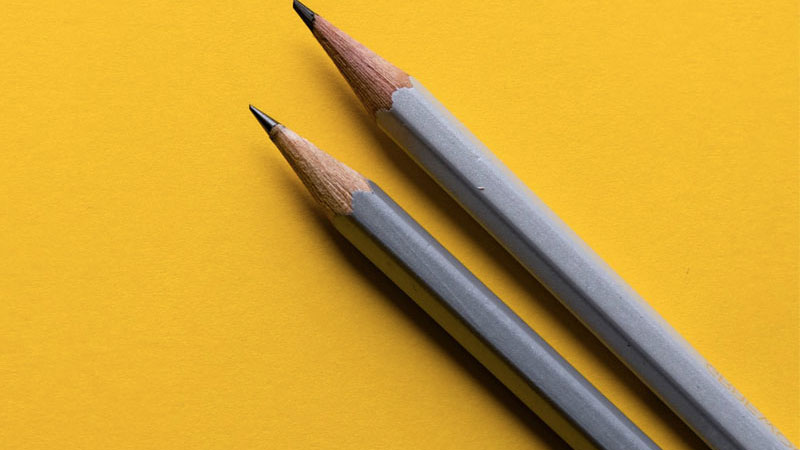 Two sharp grey pencils rest on the far right side of an all yellow backdrop.