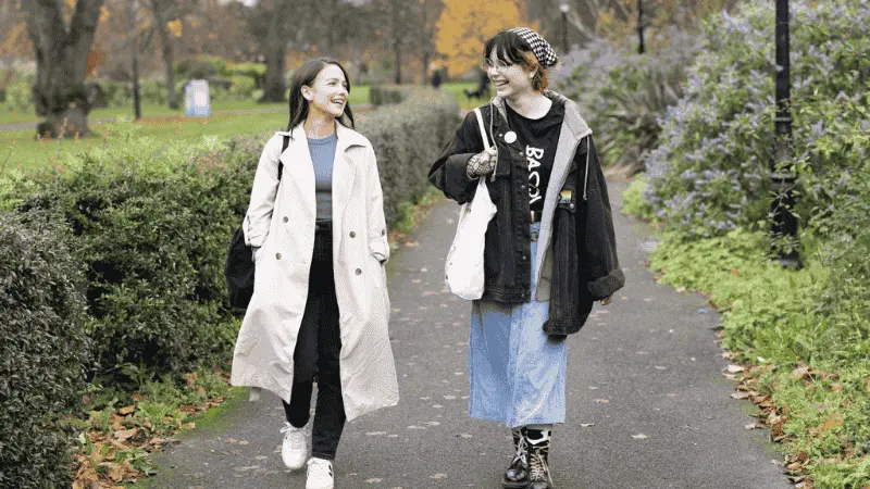 Two girls walking through the park laughing