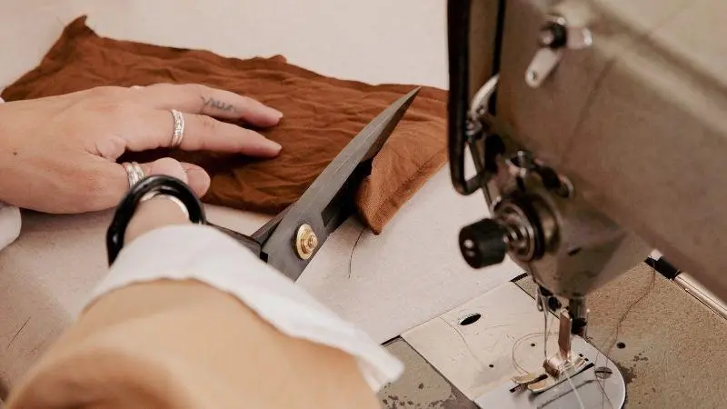 A person cutting fabric by a sewing machine