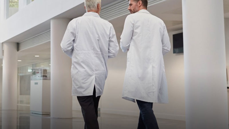 Two male health workers wearing white lab coats walking through The Spark