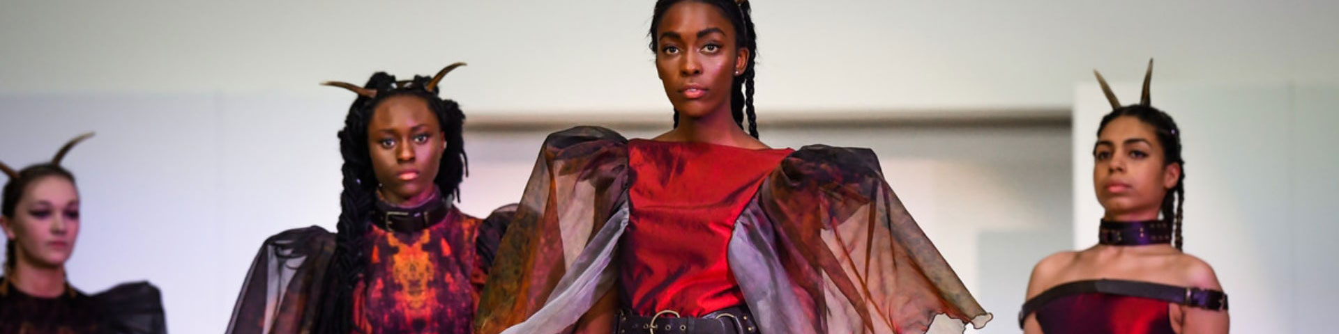 Four women in copper colour clothes walk down a catwalk.