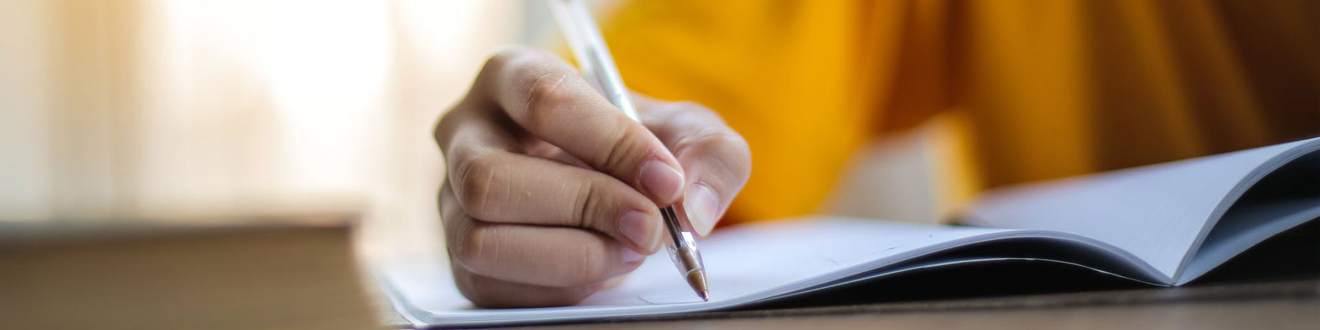 A close up of a human right hand holding a pen writing on a booklet.
