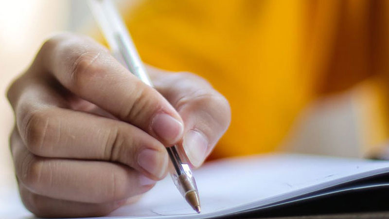 A close up of a human right hand holding a pen writing on a booklet.