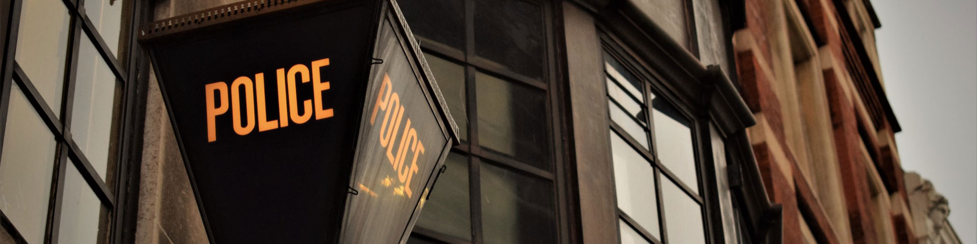 A street light with the word police written on it stands in front of an old building.