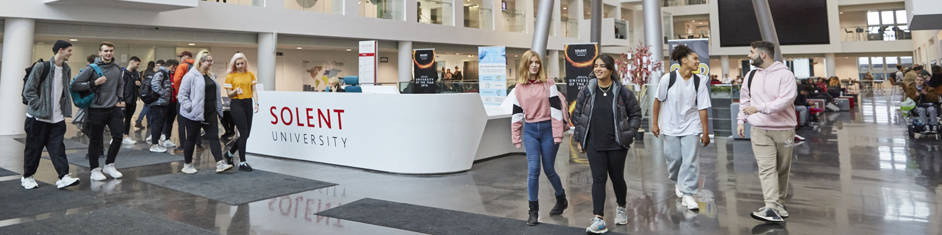 Groups of students walk around the inside of a Solent University building.