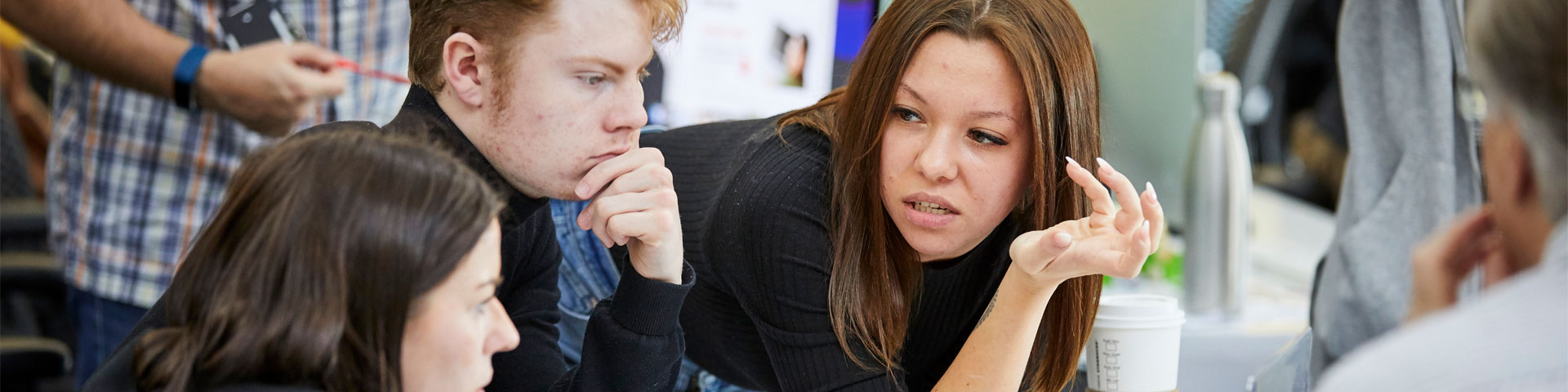 Three people sat down in a room wearing black clothes looking at each other in conversation