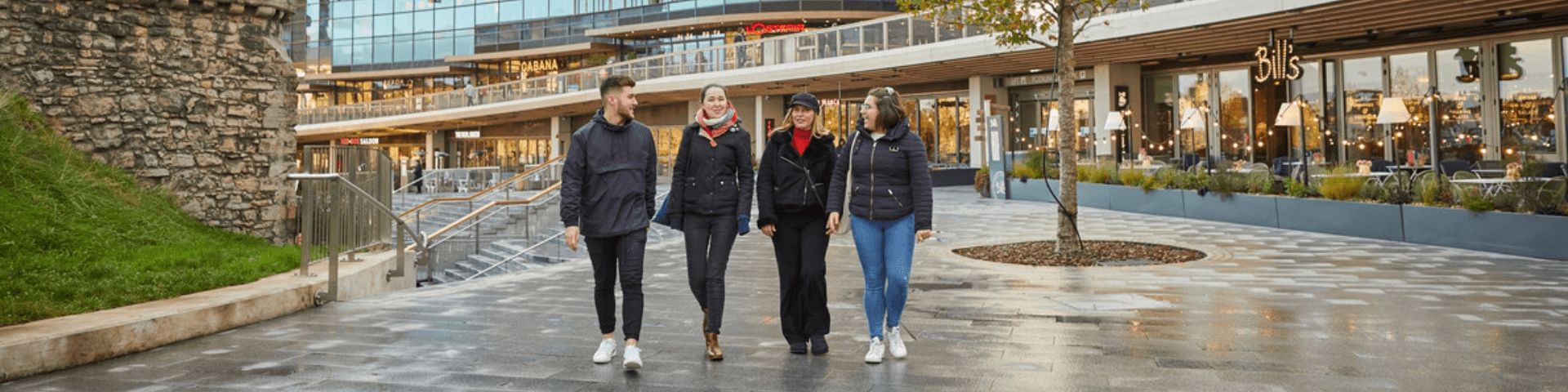 Four friends walk through Southampton city centre near to restaurants and old walls.