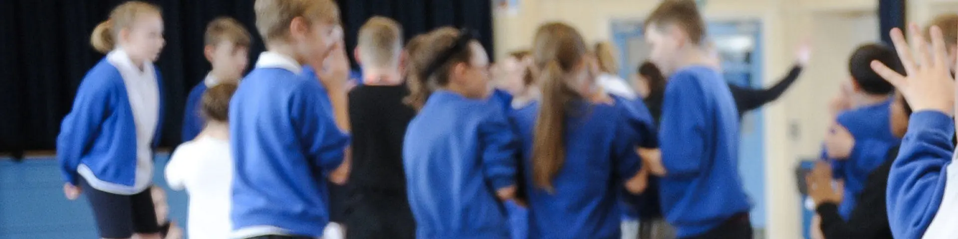 A group of young school children wearing blue sweaters taking part in a class