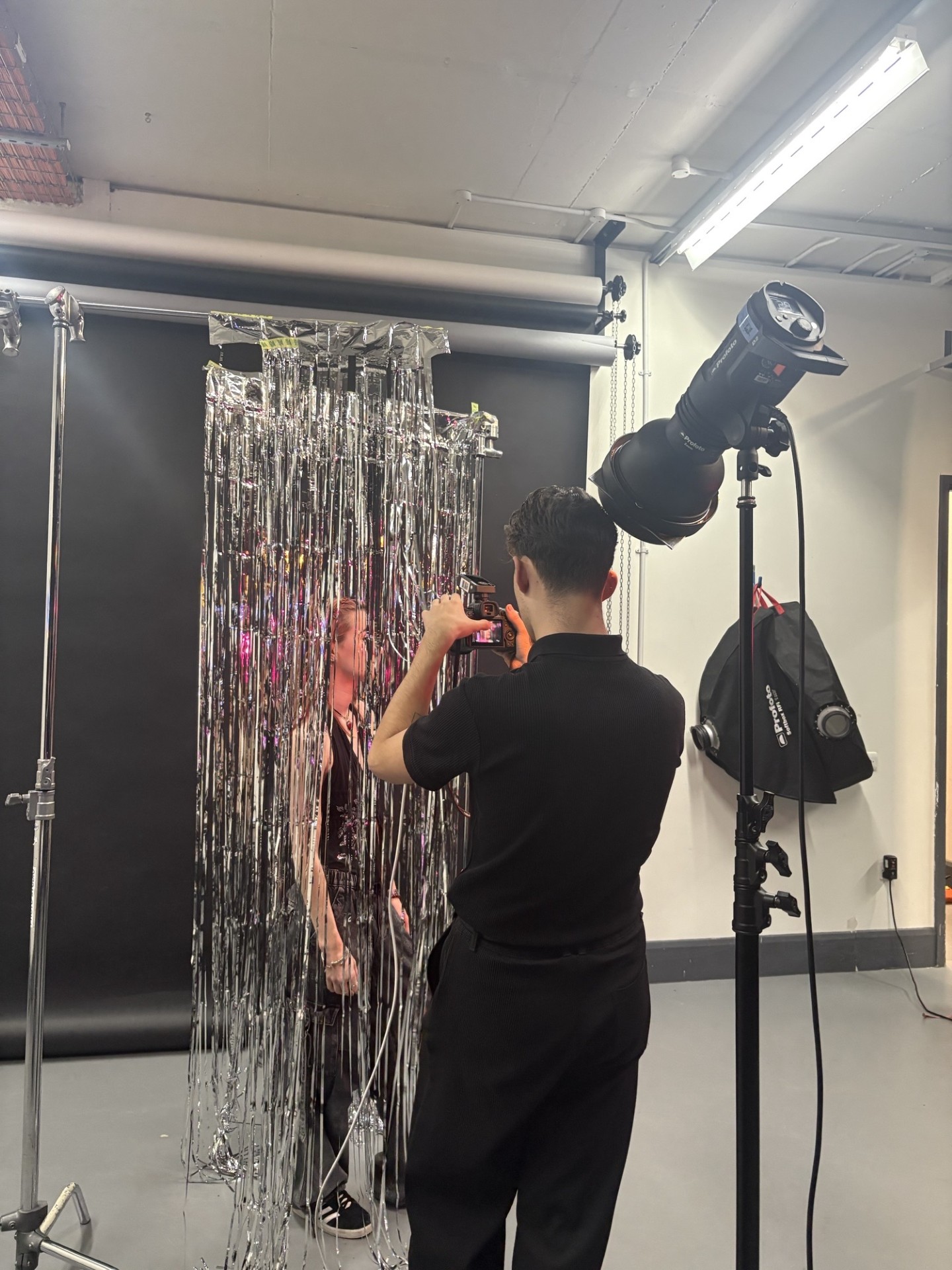 A person is being photographed behind silver tinsel in a studio with professional lighting equipment.