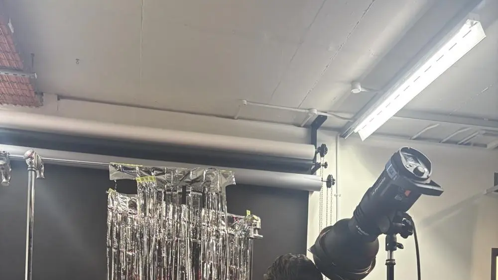 A person is being photographed behind silver tinsel in a studio with professional lighting equipment.