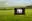 A projection stand in a field with a image of a man in a window 