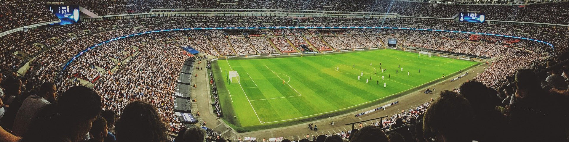 A football stadium with players on the pitch and a full crowd of supporters