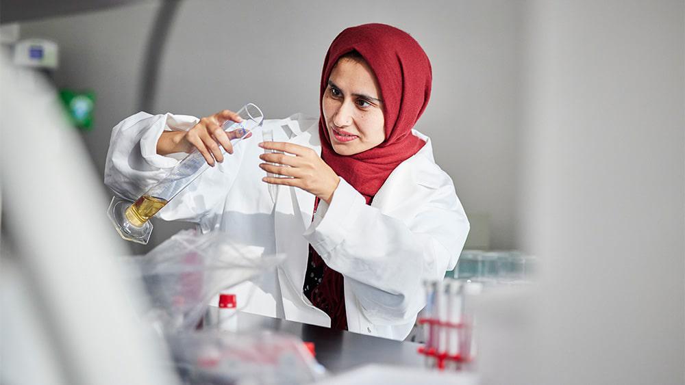 A Biomedical Science student in a laboratory, holding a beaker with fluid in it.