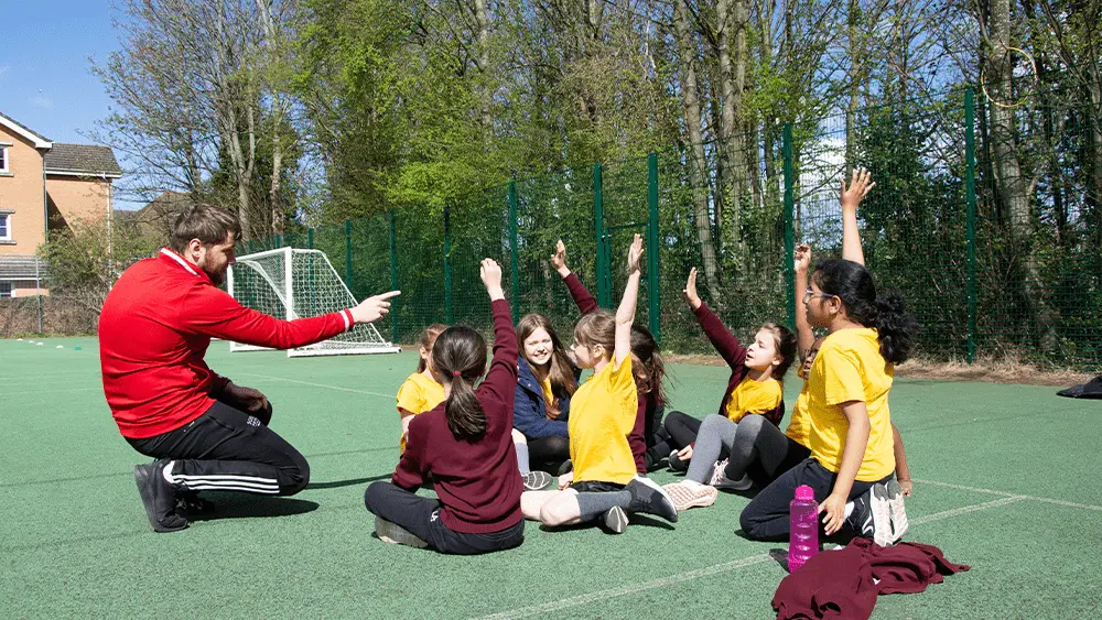 A student coaching primary school children outdoors.
