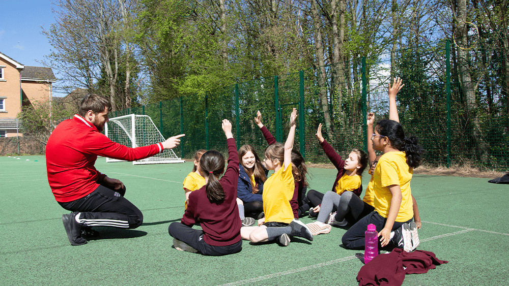 A student coaching primary school children outdoors.