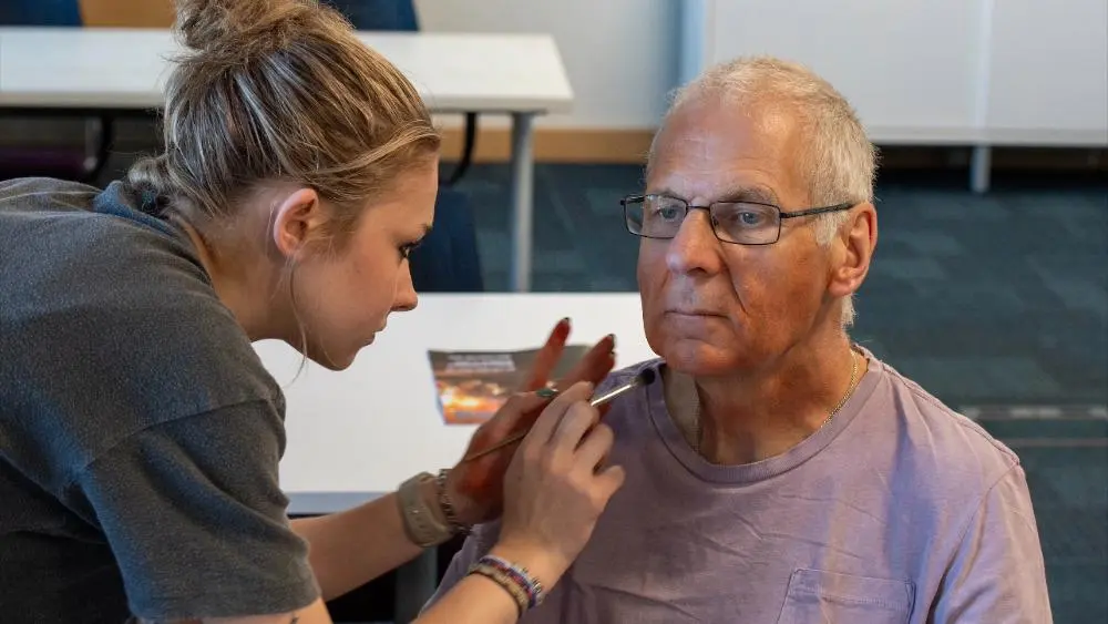 Katie Upton putting makeup on an actor to look like burns