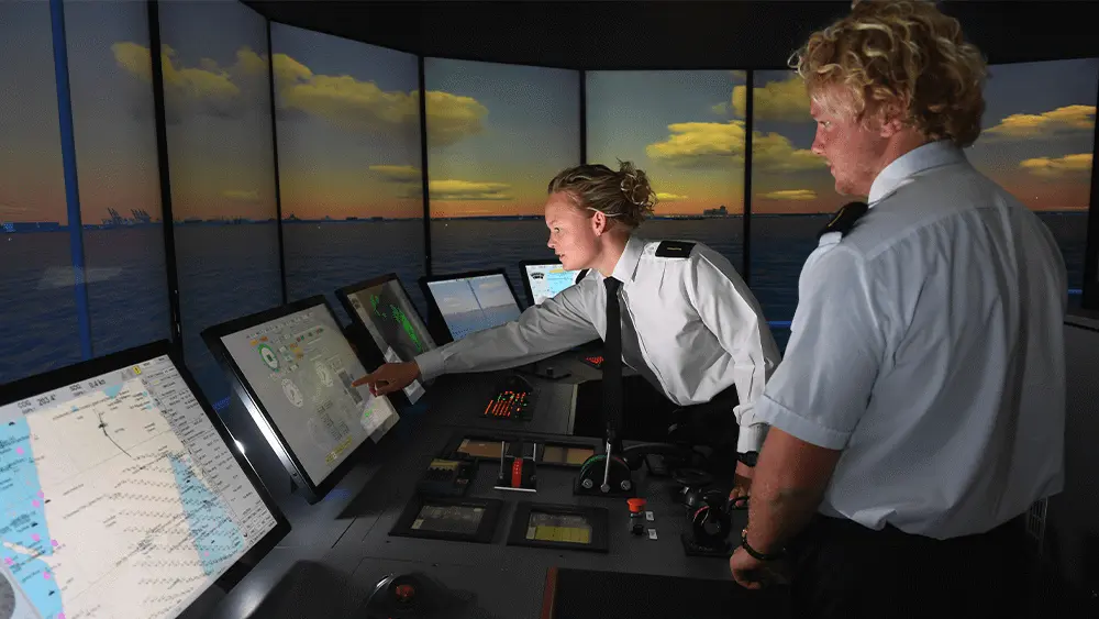 Two cadets stood at a control panel in the simulated bridge of a ship.