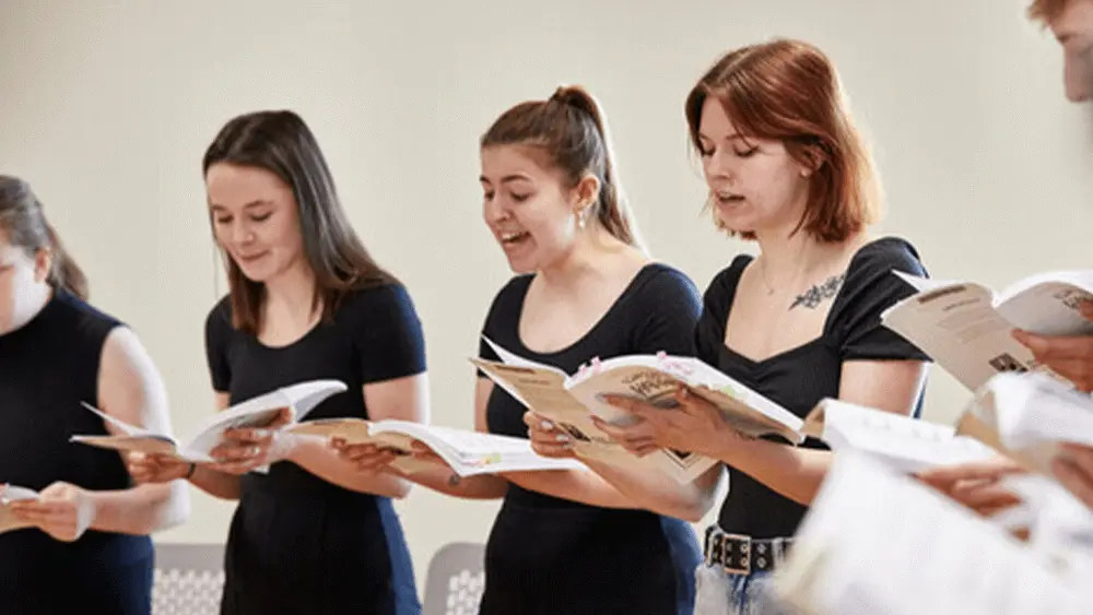 Students at Solent University singing together from lyric books.