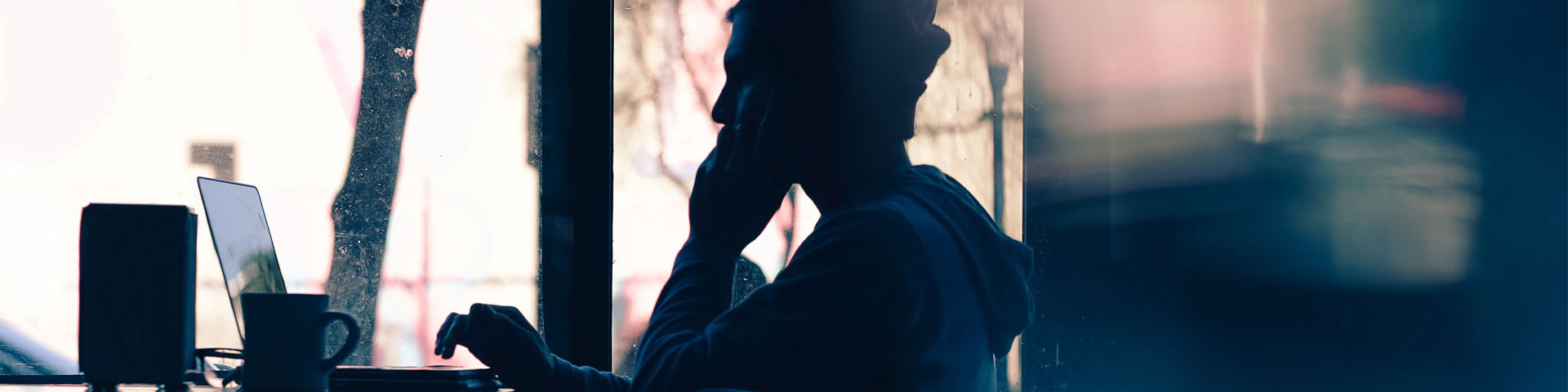 Silhouette of a person looking at a laptop in a cafe