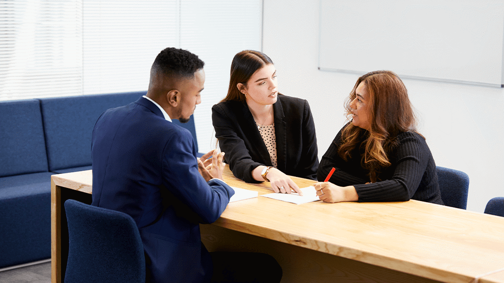 3 people sat at a desk with two of them offering advice