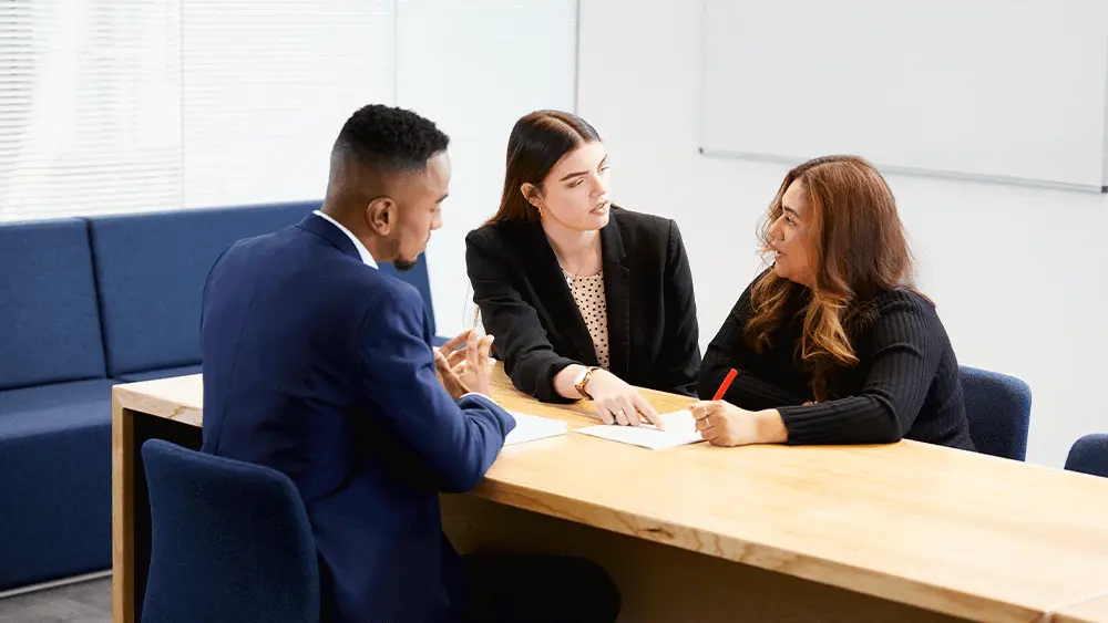 A man and two women sat together at a table, looking through a form.