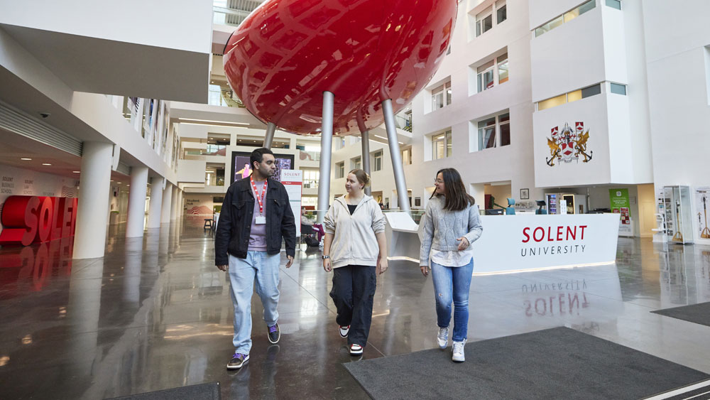Three students walking through the Spark atrium with the pod behind them