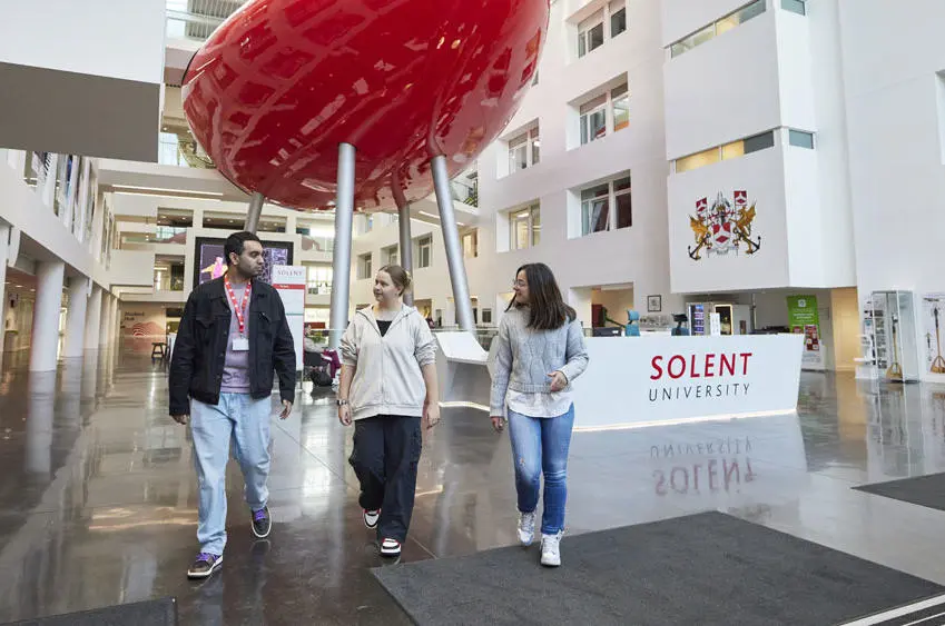 Three students walking through the Spark atrium with the pod behind them