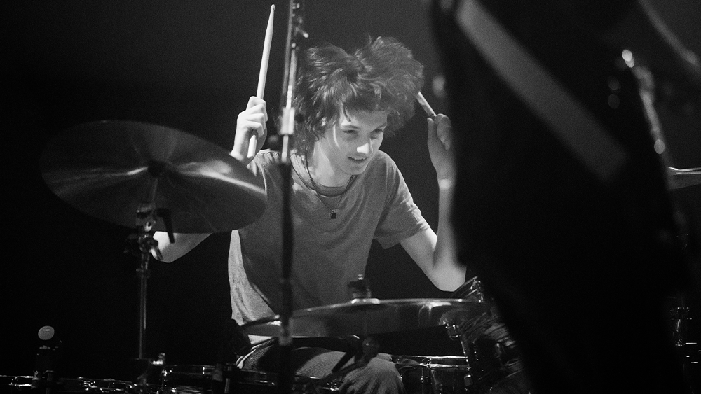 A black and white photo of a young man drumming.
