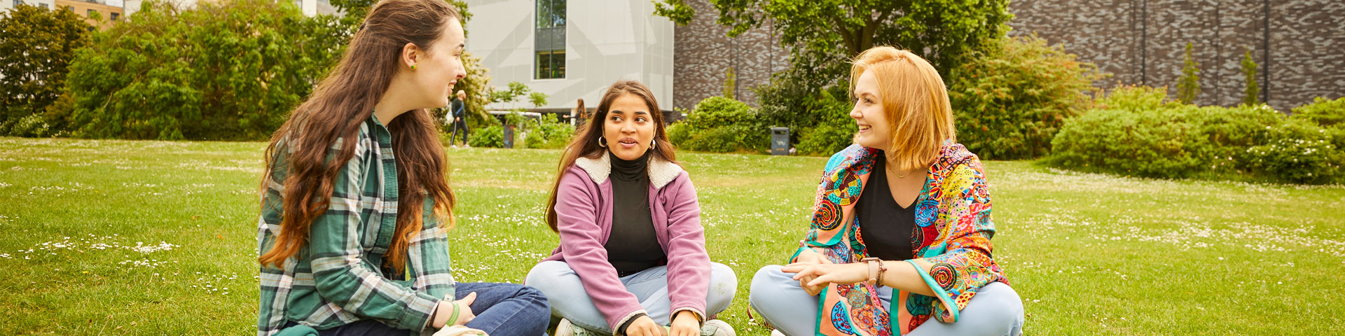 Three female students sat on the grass in the park