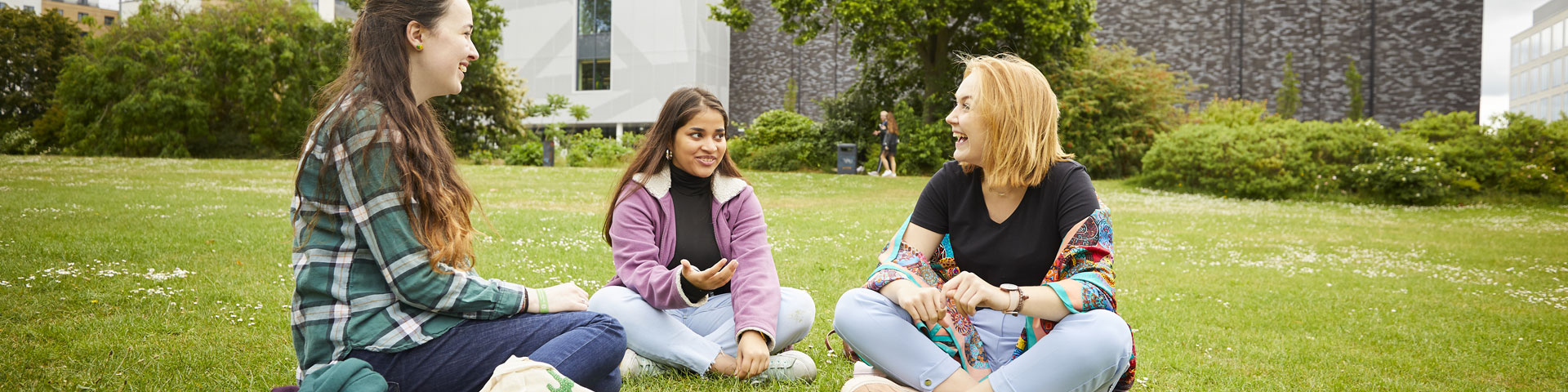 Three female students sat in the park laughing