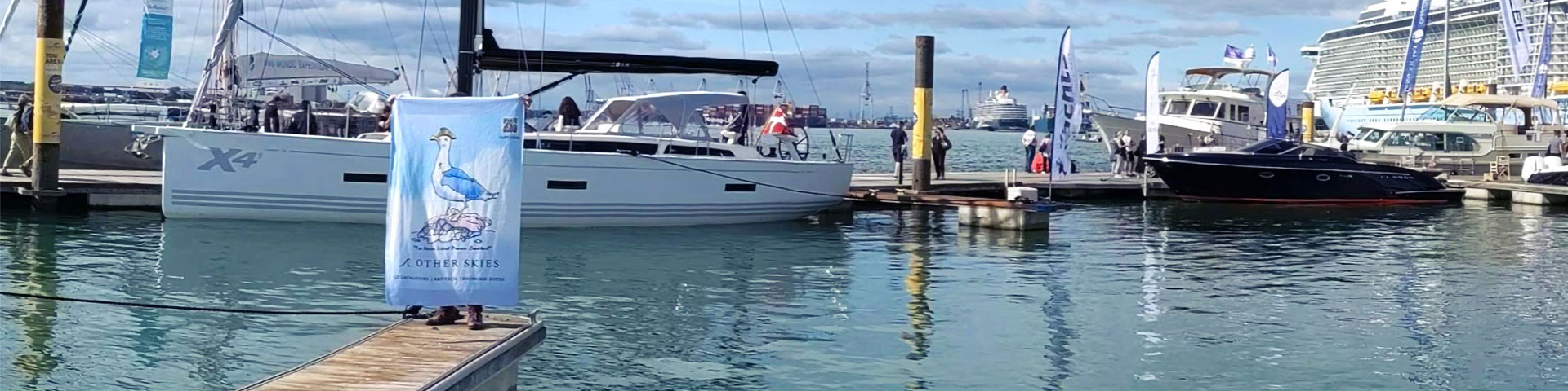 Other Skies banner being held up on a pontoon with boats in the background