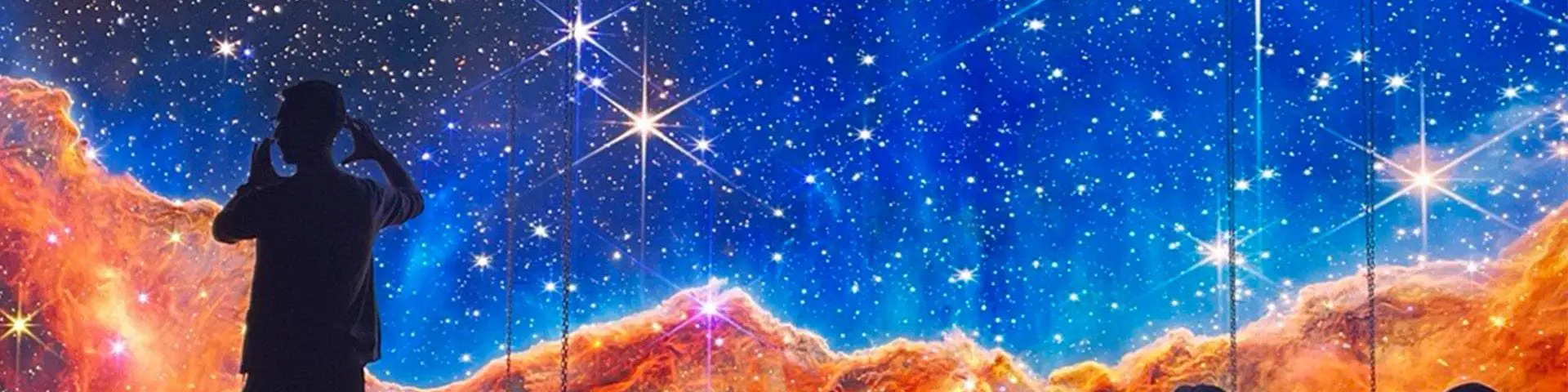 A man stands in front a screen displaying a starry sky and orange mountains.