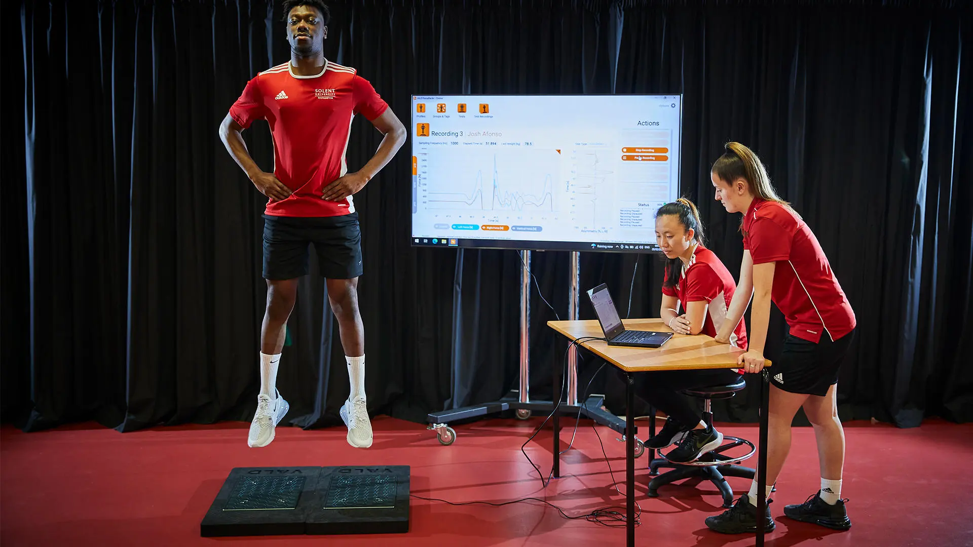 Image of student working in biomechanics lab - a male student is jumping and two female students are analysing the movement with a computer