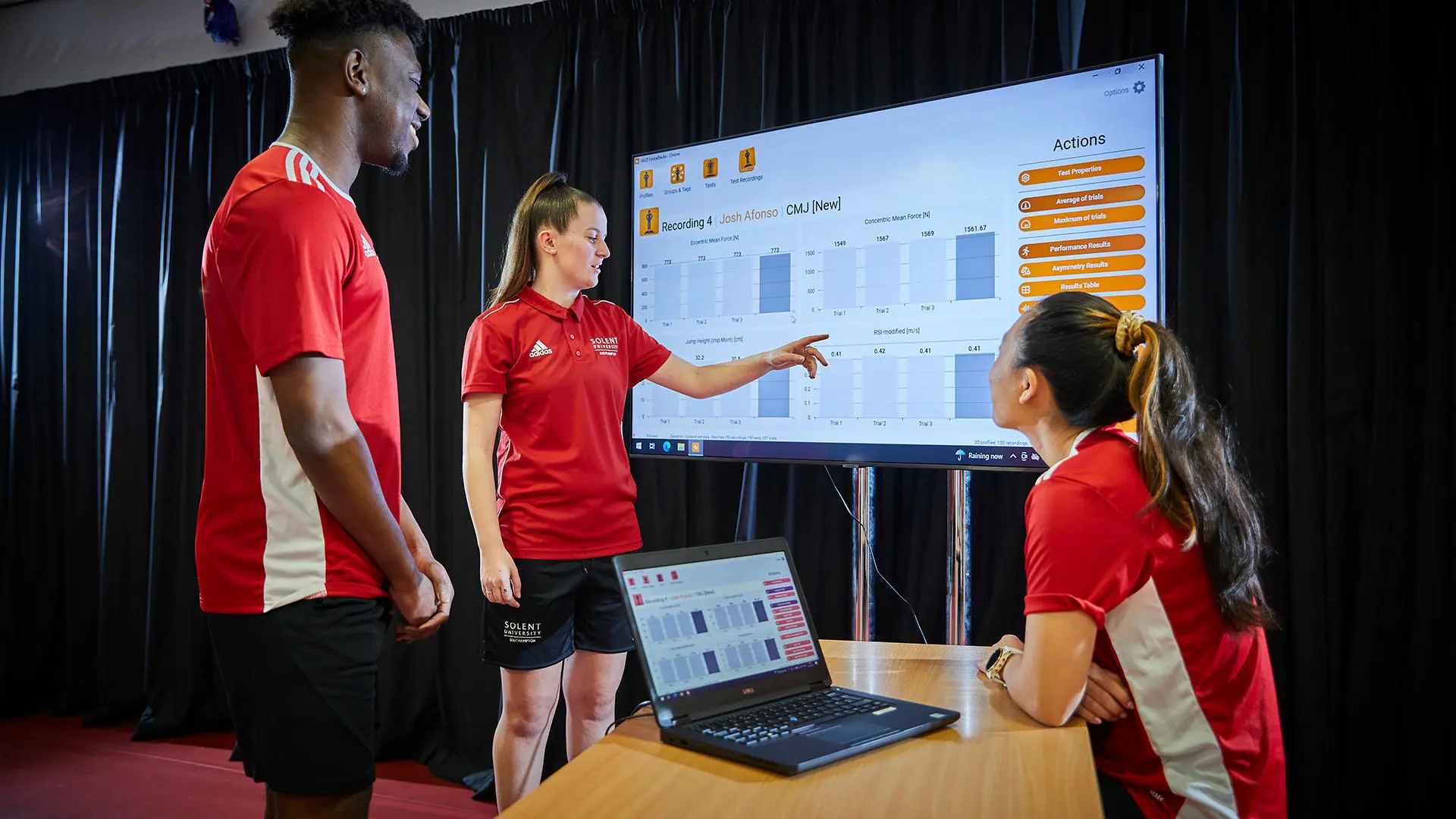Image of student working in biomechanics lab - the three students are looking at the results on a computer and large screen. 