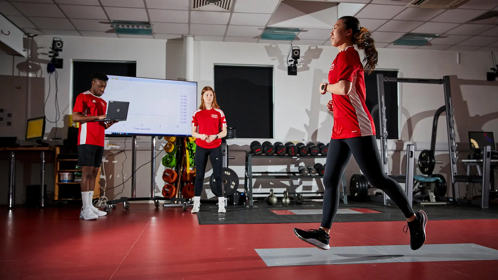 Image of student working in biomechanics lab - a female student is running and two other students are analysing the results on the computer. 