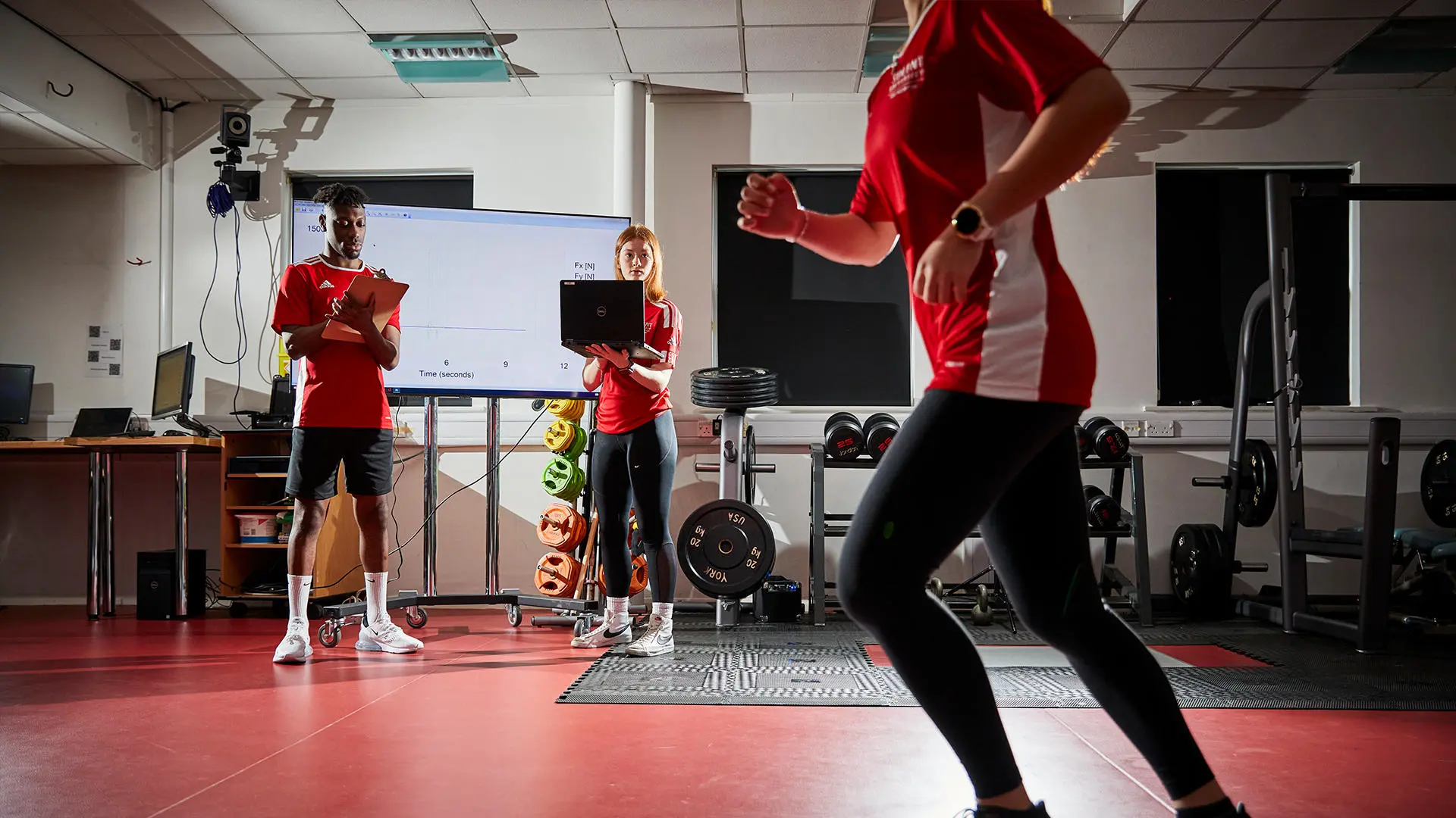 Image of student working in biomechanics lab - a female student is running and two other students are analysing the results on the computer. 