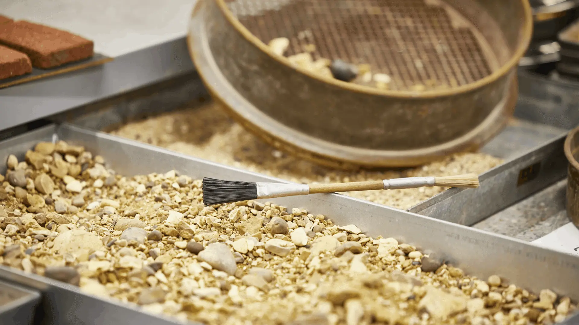 Small pieces of rubble in a tray with a brush and a sieve