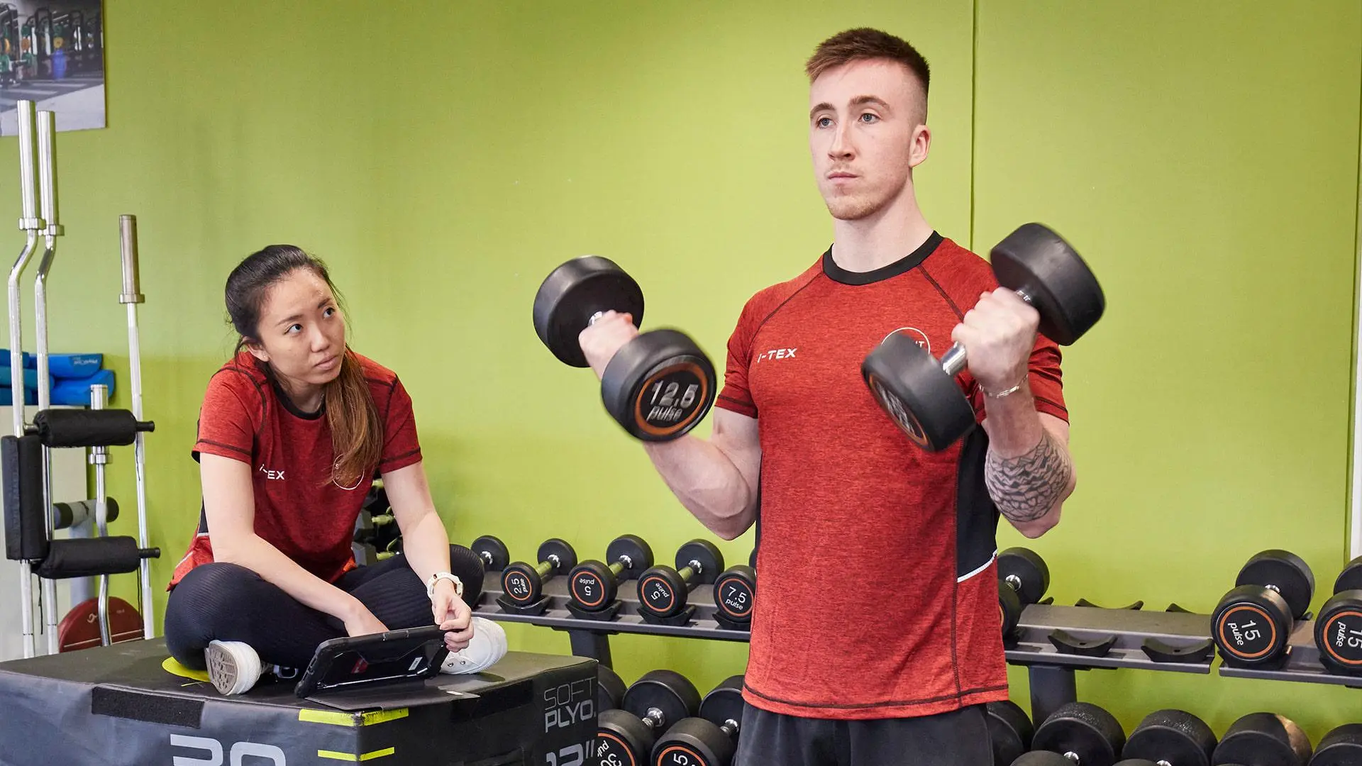 Studetn using dumbells in teaching gym supervised by another student