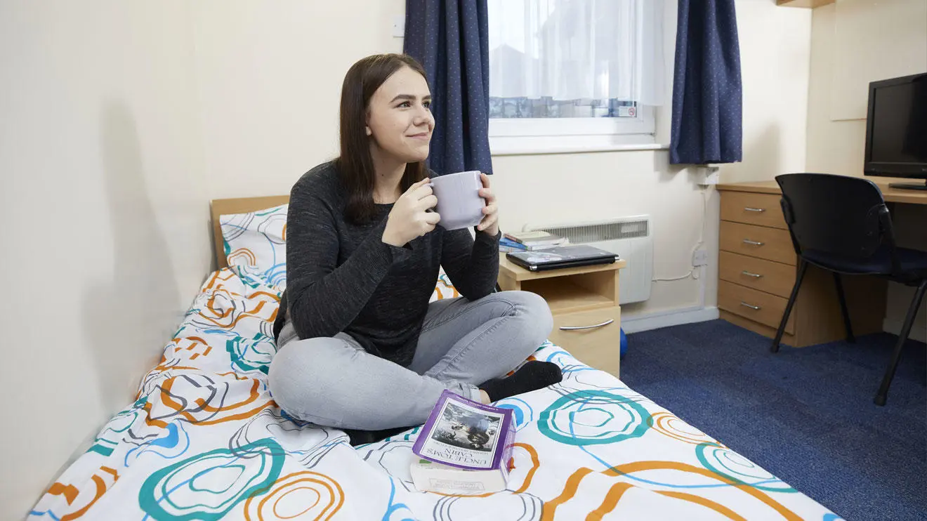A female student drinking from a mug in a room in David Moxon residence