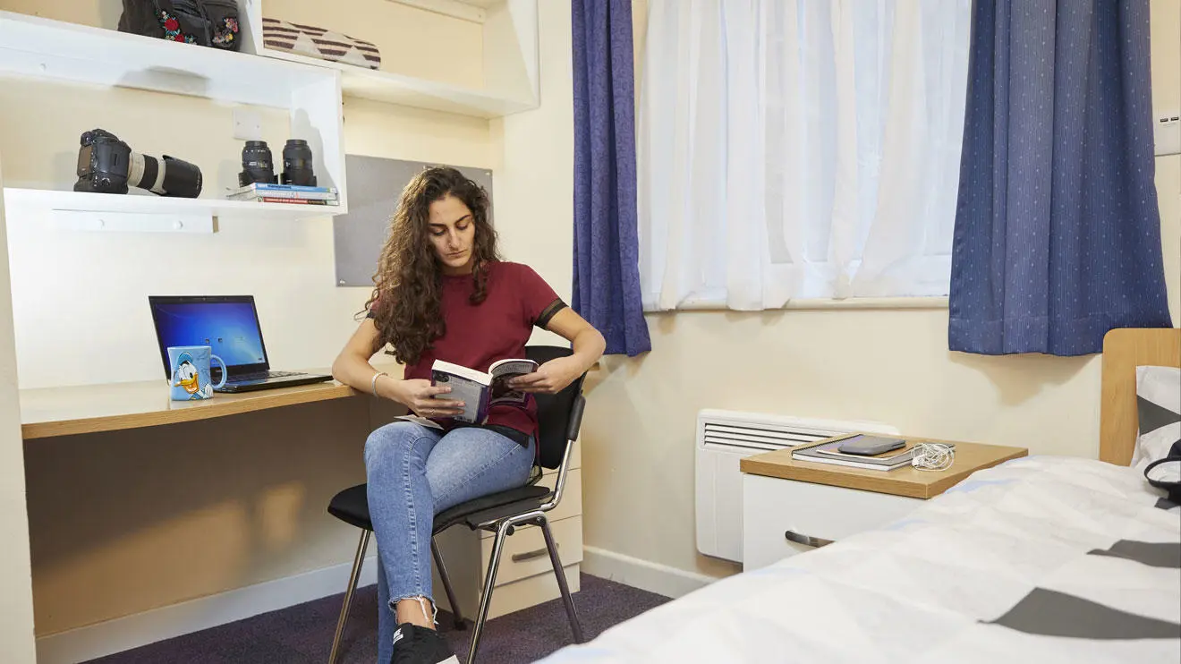 A female student reading a book in a room in Kimber residence