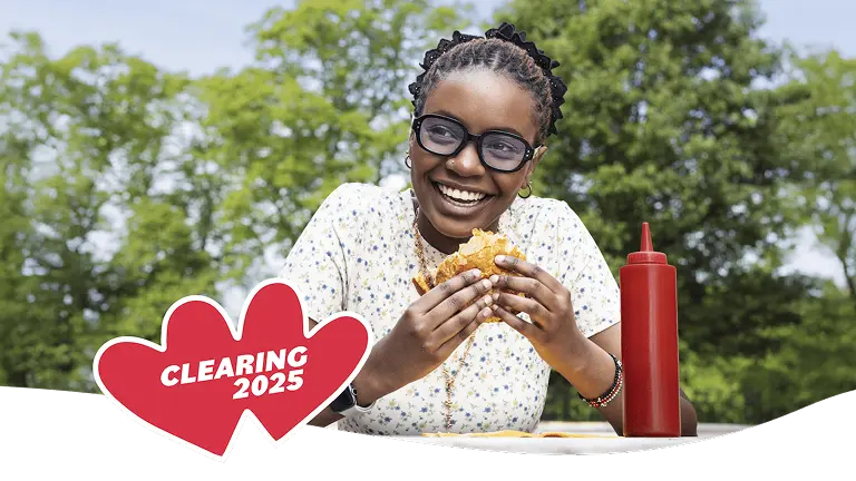 A young woman is eating a burger and smiling. There are stickers next to the image. Text says 'Clearing 2025'