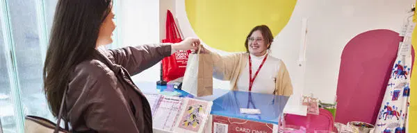 A shop assistant handing a brown paper bag to a customer