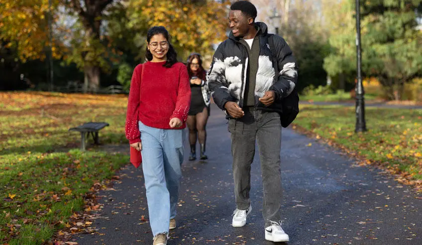 A male and female students walking through the park in autumn